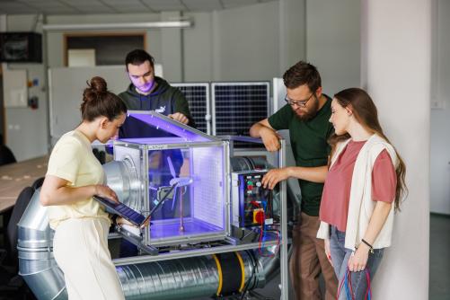 Grupa osób prowadzi zajęcia przy stanowisku laboratoryjnym z modelem systemu wentylacyjnego.